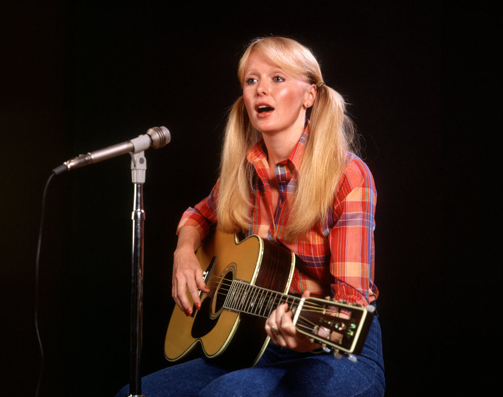 Detail of 1970s blond young woman ponytails plaid shirt jeans play guitar singing microphone folk singer singers by Anonymous