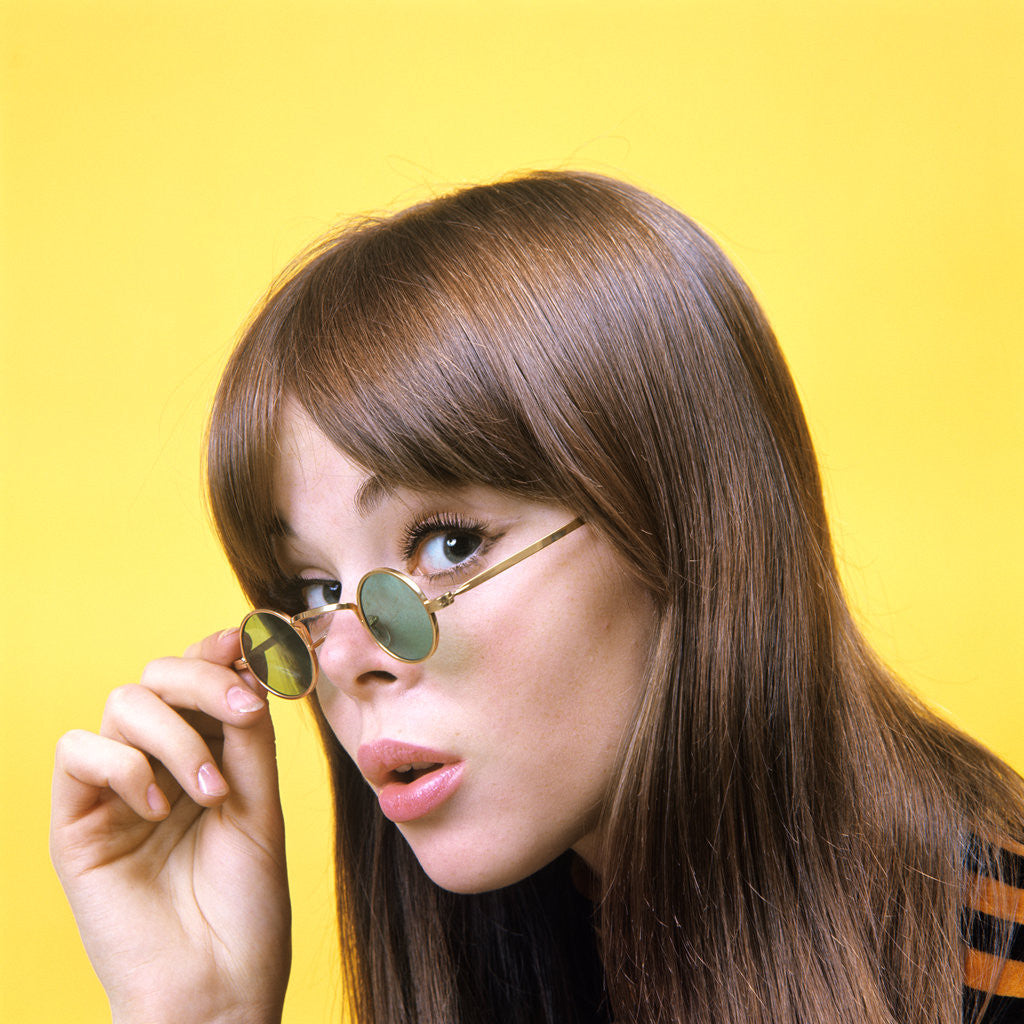 Detail of 1960s portrait young brunette woman wear granny sunglasses surprised doubtful facial expression yellow background by Anonymous