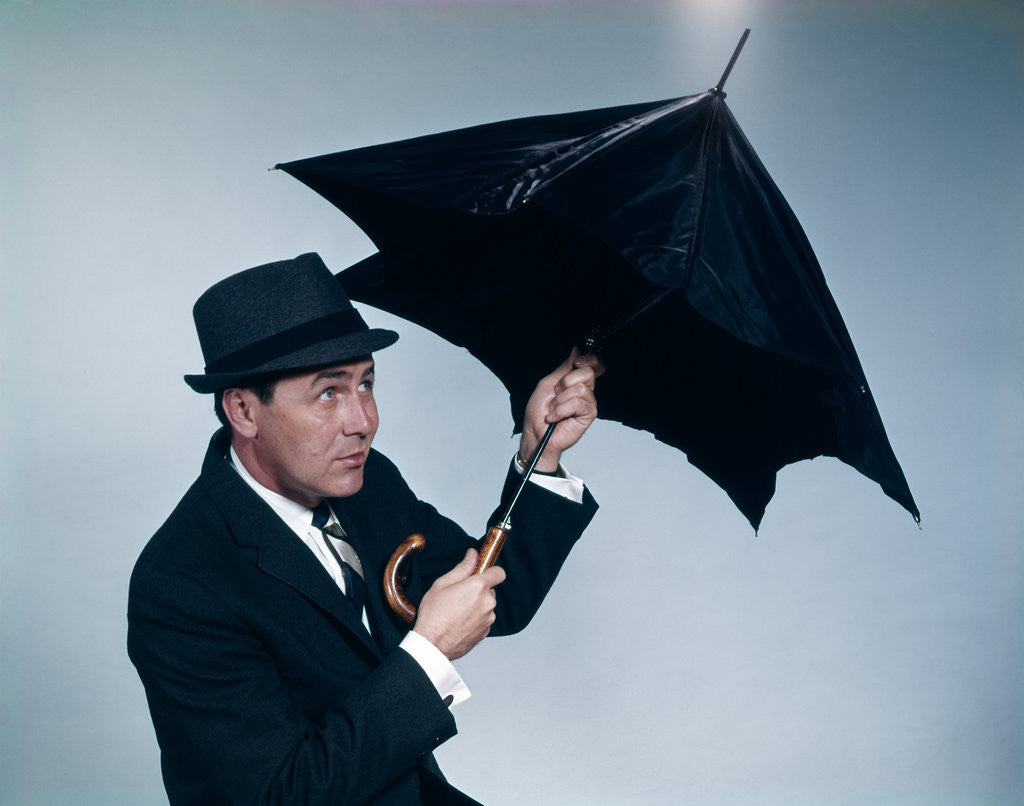 Detail of 1960s businessman wearing hat opening umbrella to protect from rain by Anonymous