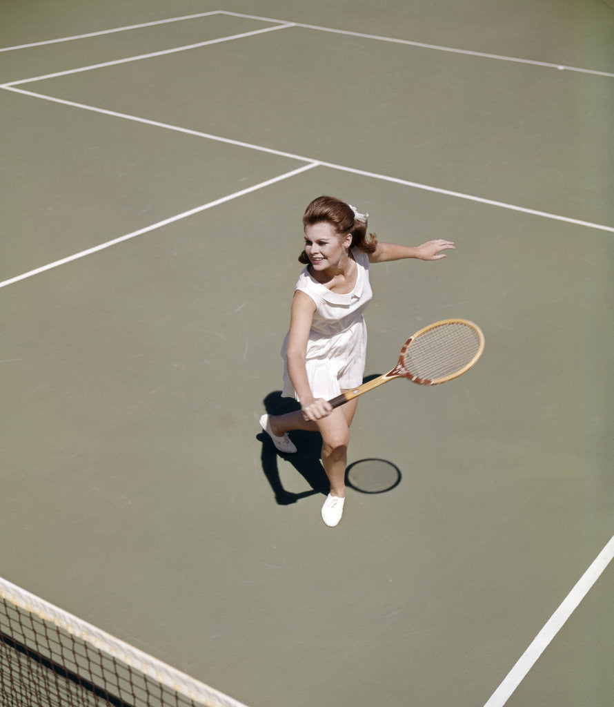 Detail of 1960s smiling woman playing tennis swinging wood racket to hit ball by Corbis
