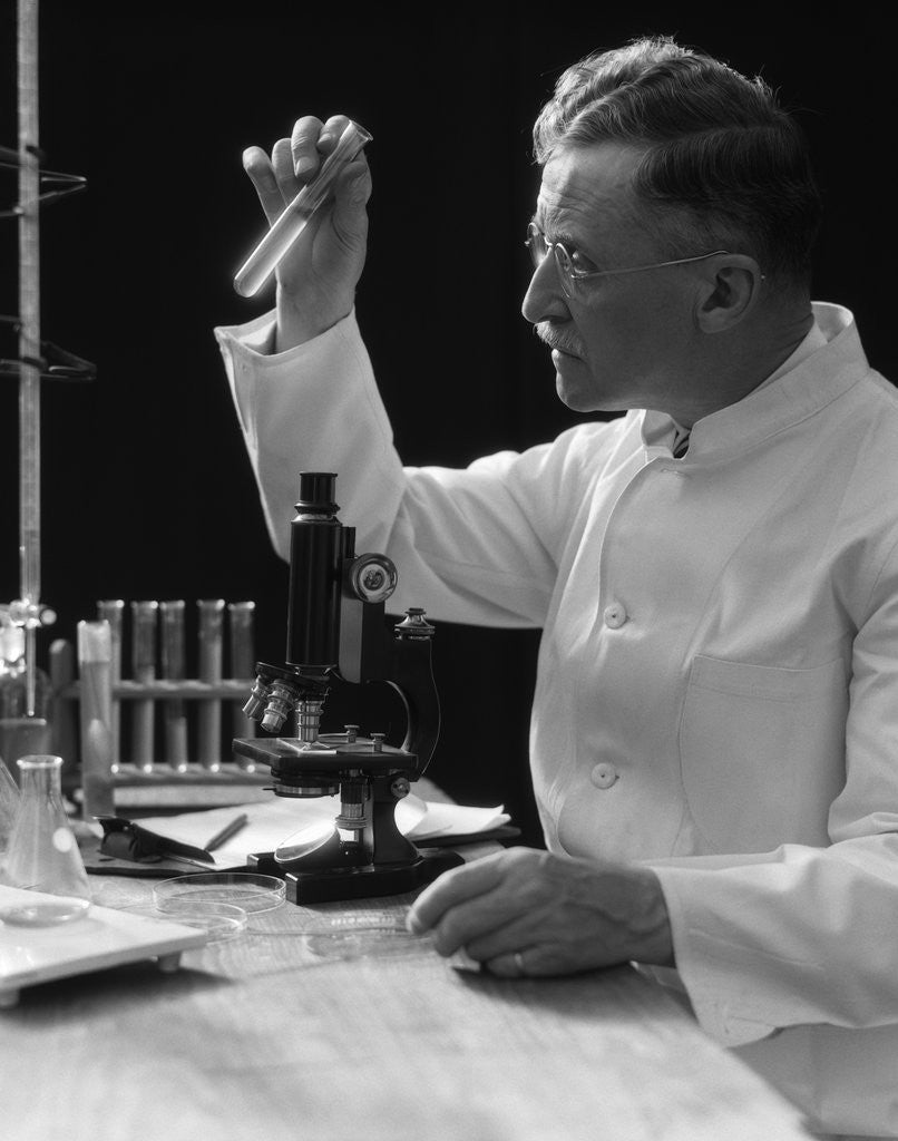 Detail of 1920s 1930s 1940s scientist lab technician in white coat looking at test-tube in front of microscope by Anonymous