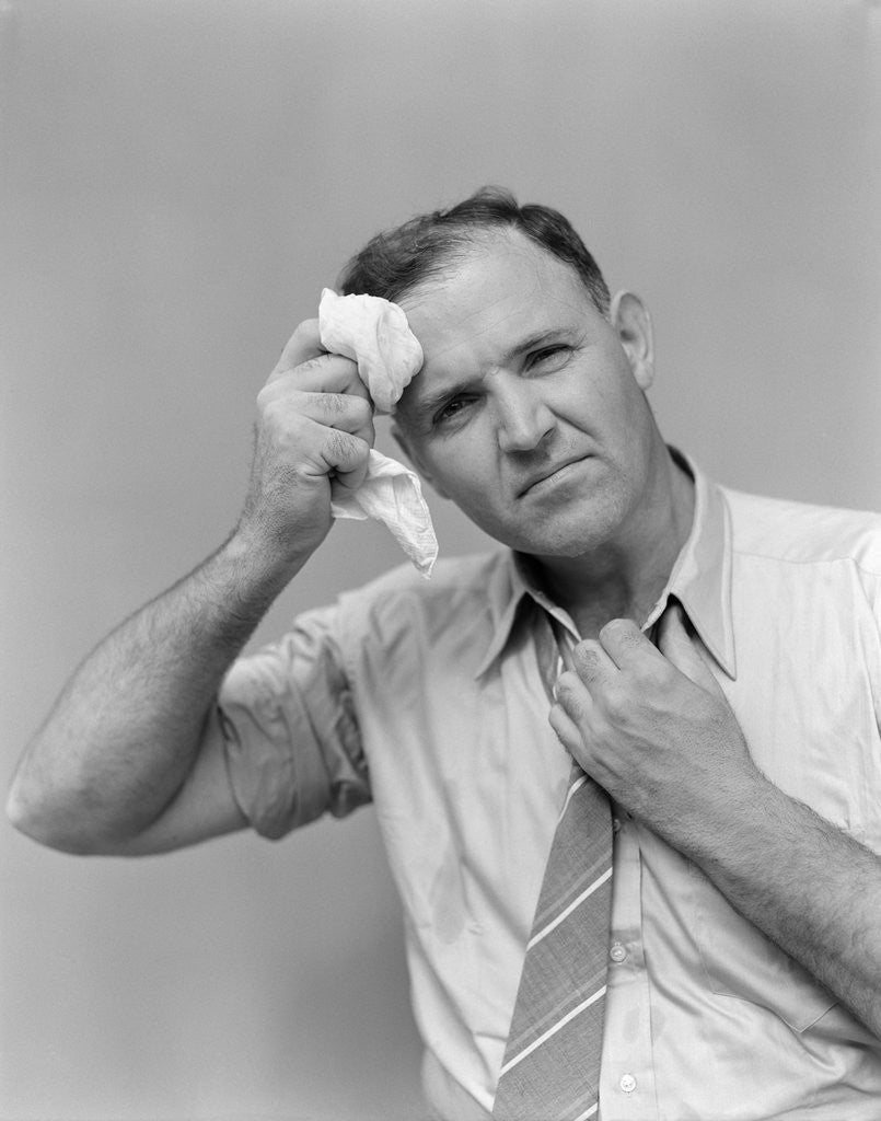 Detail of 1940s 1950s perspiring man in rolled up shirt sleeves loosening tie holding handkerchief wiping forehead looking at camera by Anonymous