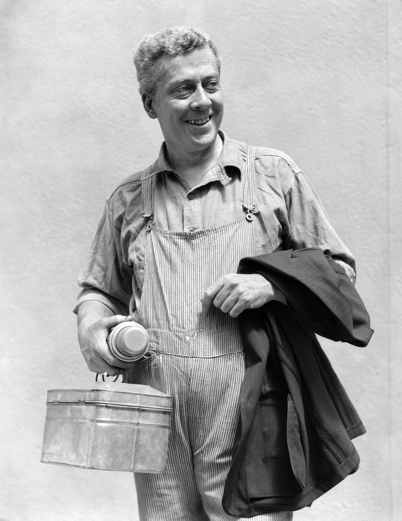 Detail of 1930s man in overalls work uniform holding thermos lunchbox and jacket by Anonymous