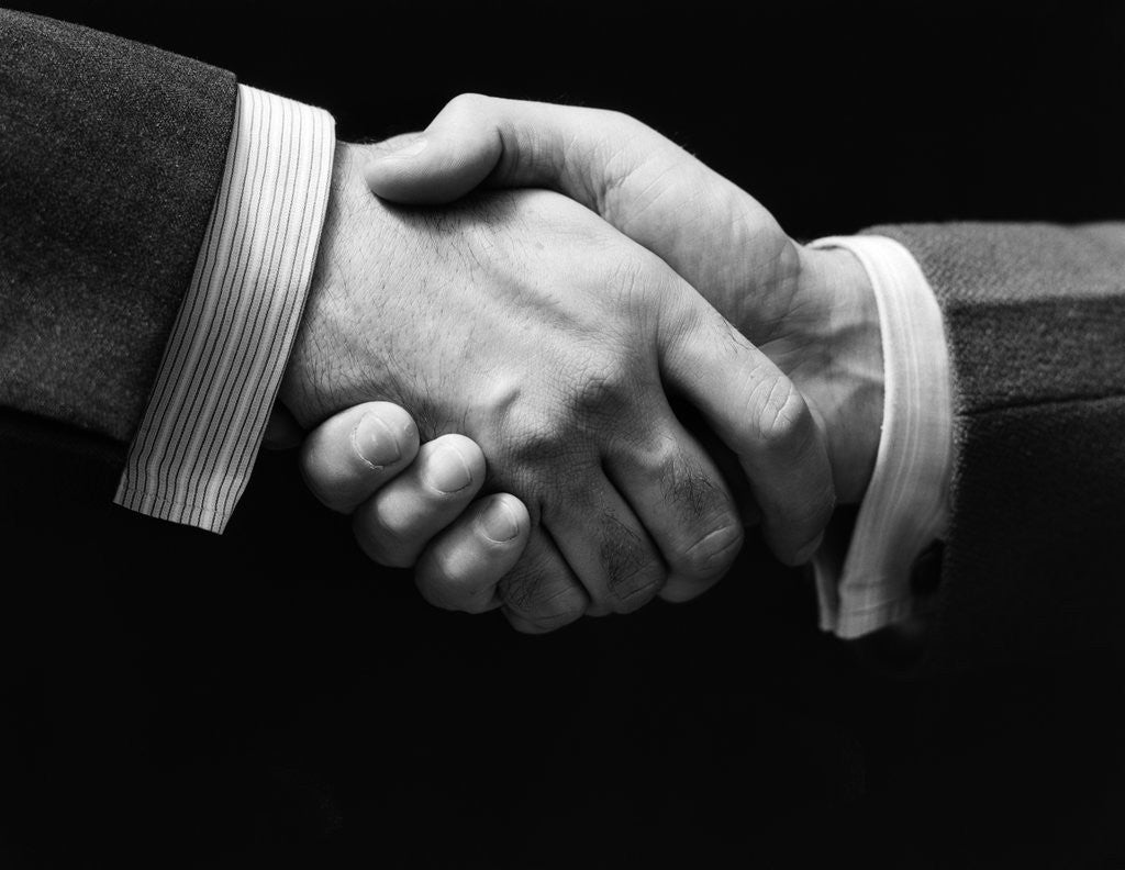 Detail of 1930s close-up of businessmen's hands in handshake against dark background by Corbis