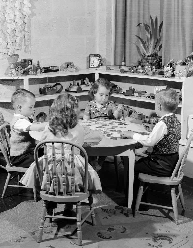 Detail of 1950s 4 pre-school age children seated at small round table putting together jigsaw puzzle by Anonymous