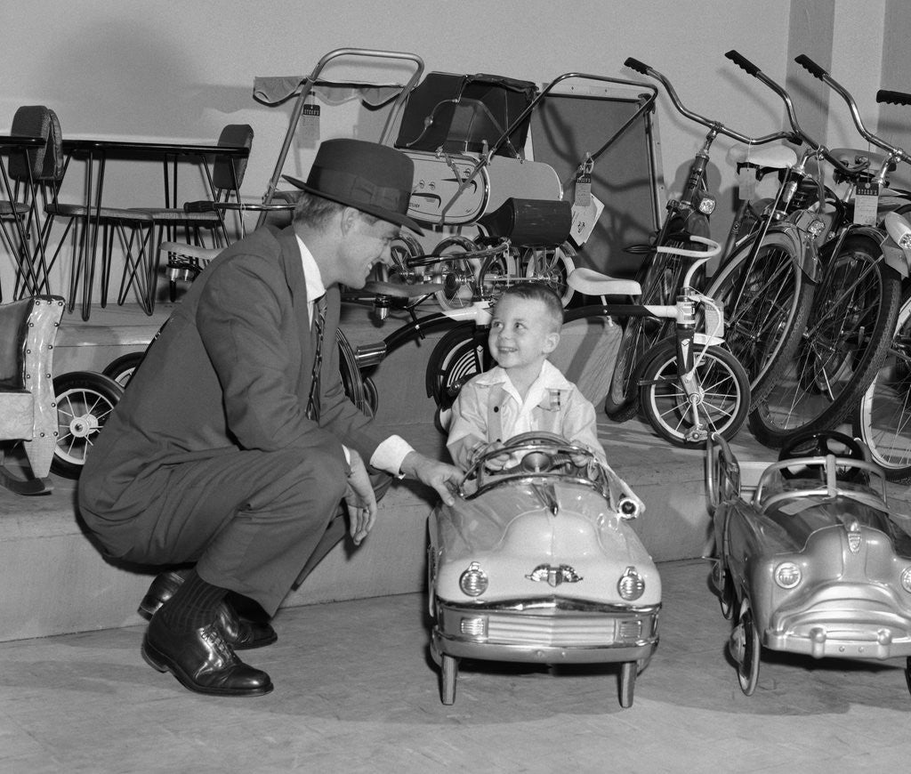 Detail of 1950s father in toy store purchasing for son driving toy convertible peddle car by Corbis