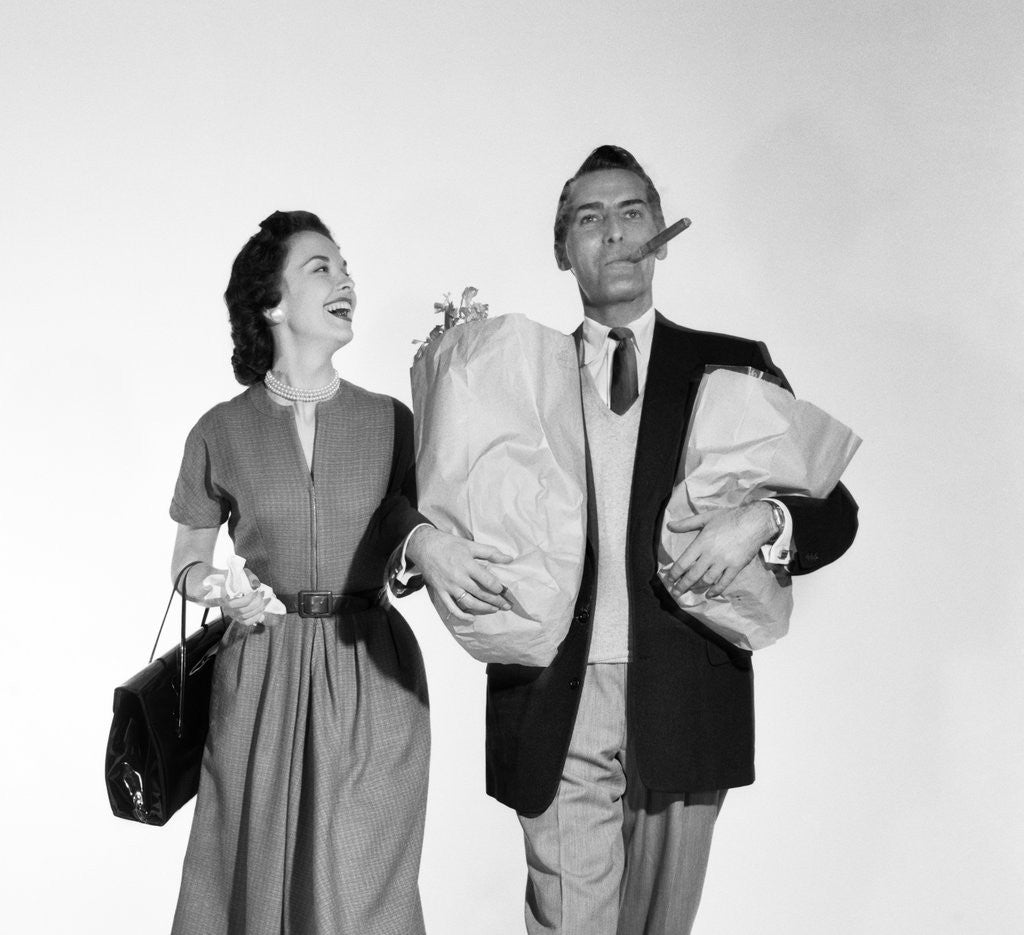 Detail of 1950s couple walking woman smiling at man carrying grocery bags smoking cigar by Anonymous