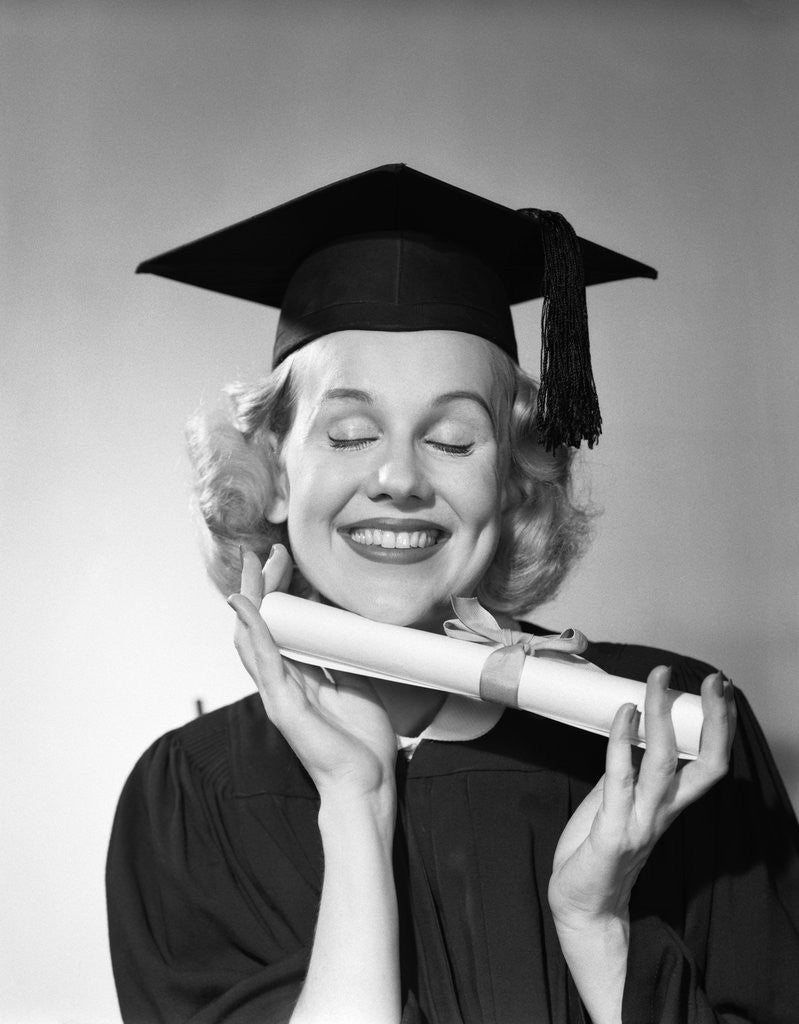 Detail of 1950s smiling woman teenage girl eyes closed holding diploma graduate wearing cap gown by Anonymous