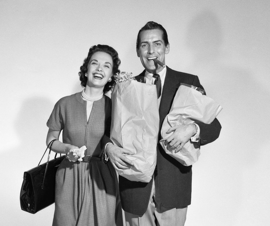 Detail of 1950s couple smiling woman man carrying grocery bags smoking cigar looking at camera by Anonymous