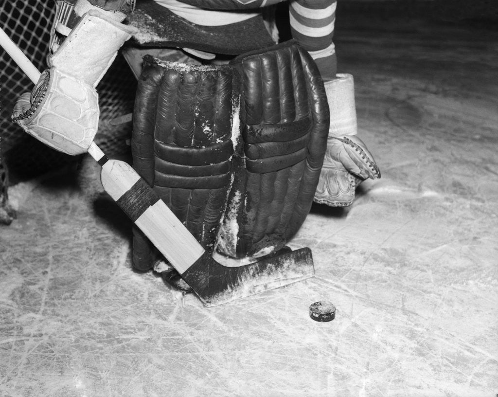 Detail of 1940s 1950s close-up of padded goalie shown waist-down holding stick with puck in front of him by Anonymous