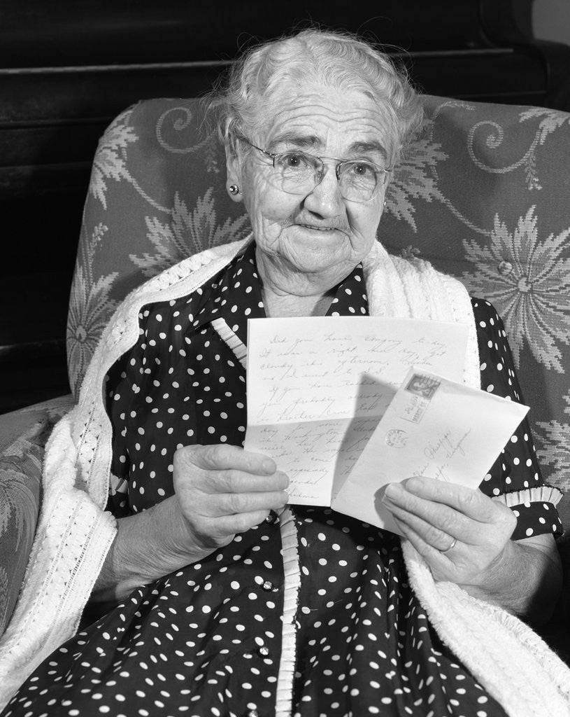 Detail of 1960s elderly woman in polka-dotted dress & shawl reading letter by Corbis