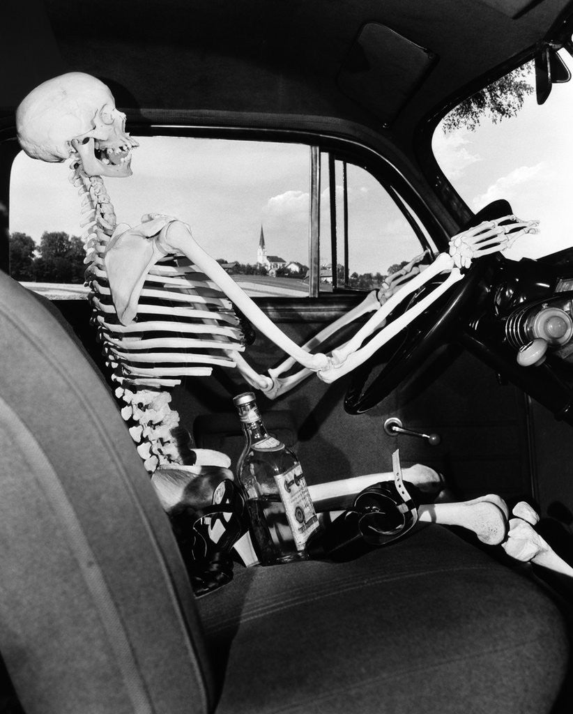 Detail of 1930s 1940s still life of skeleton driving car with whiskey bottle and woman's shoes on seat beside it by Corbis
