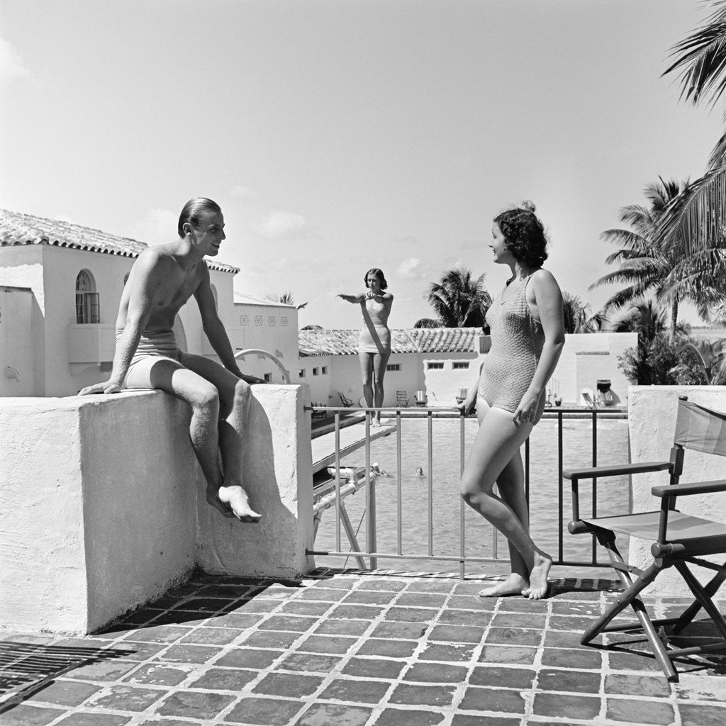 Detail of 1930s man woman wearing bathing suits on terrace overlooking swimming pool woman on diving board by Anonymous