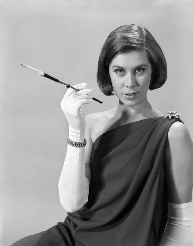 Detail of 1960s formally elegantly dressed young woman looking at camera with a cigarette holder wearing long white gloves by Anonymous