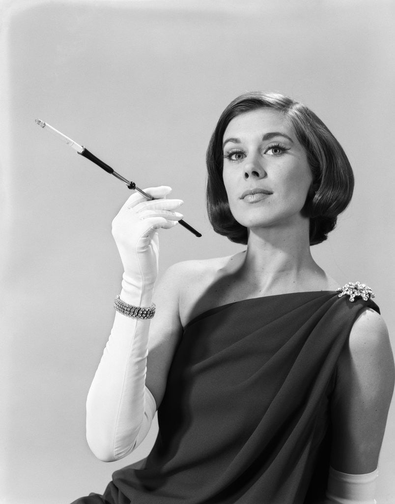 Detail of 1960s formally elegantly dressed young woman arrogant expression holding long cigarette holder wearing long white gloves by Anonymous