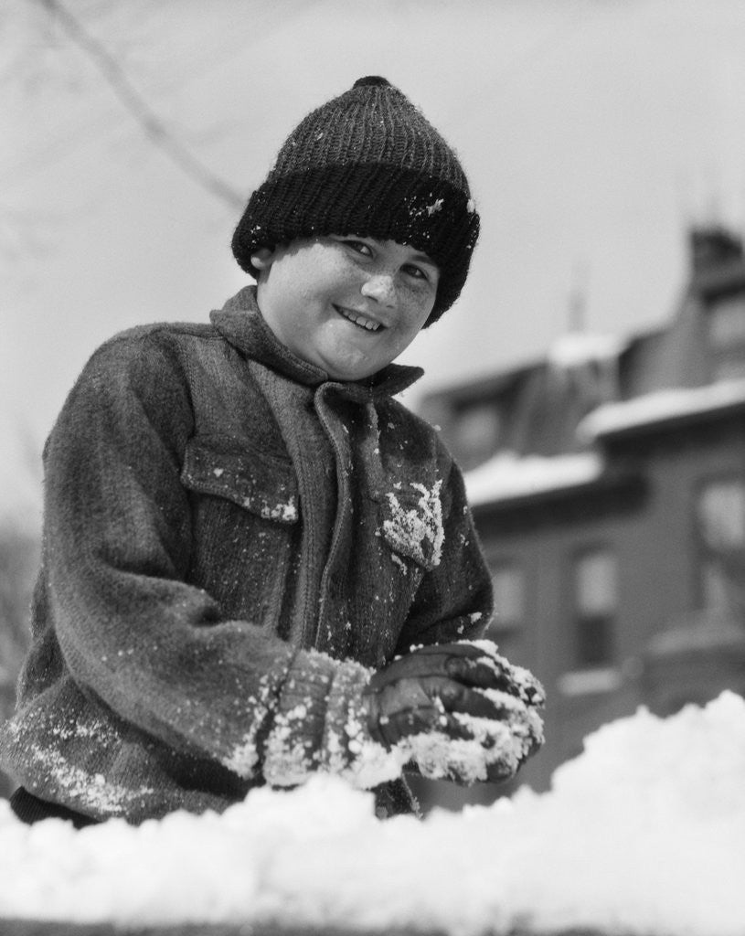 Detail of 1920s 1930s smiling boy playing in snow making snowball looking at camera by Anonymous