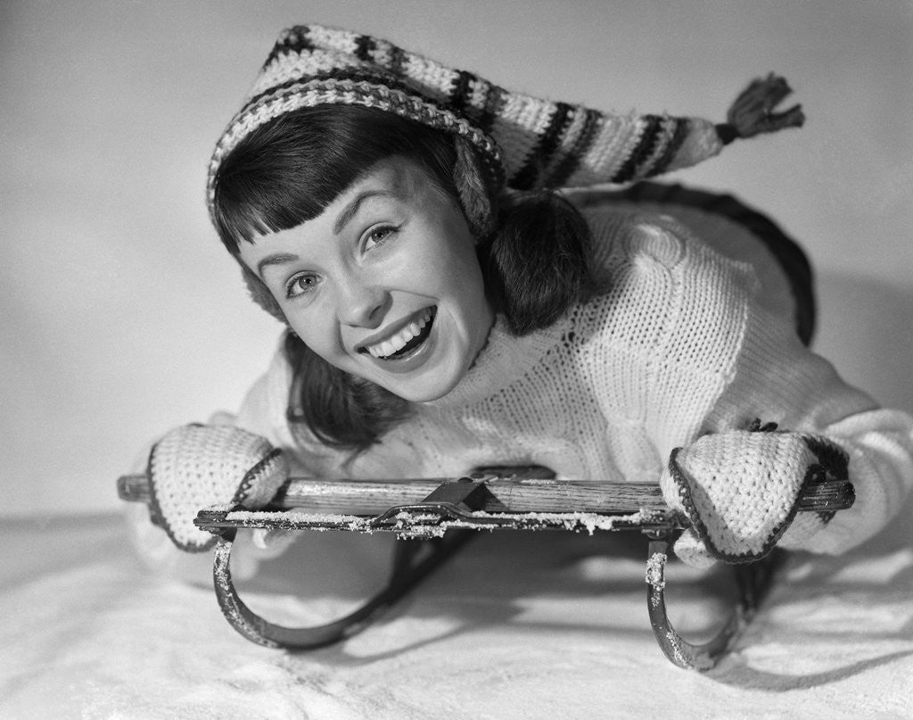 Detail of 1950s smiling young teenage woman posing on sled in winter wool knit clothes looking at camera by Corbis