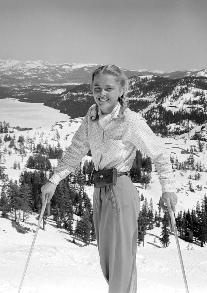 Detail of 1940s 1950s young blond athletic woman looking at camera smiling standing with ski poles top of mountain by Anonymous