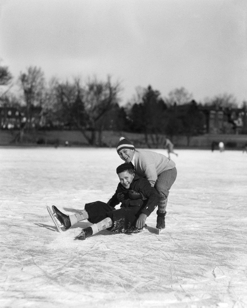Detail of 1920s 1930s two smiling boys looking at camera ice skating one boy fallen other picking him up by Anonymous