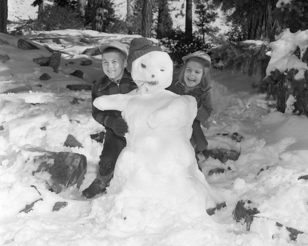 Detail of 1950s 1960s smiling boy and girl building a snowman together in snowy woods by Anonymous