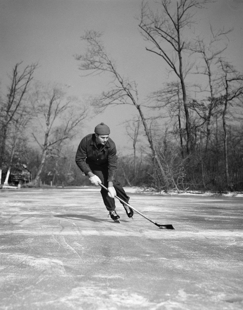 Detail of 1940s man playing ice hockey on frozen lake controlling puck with stick by Anonymous