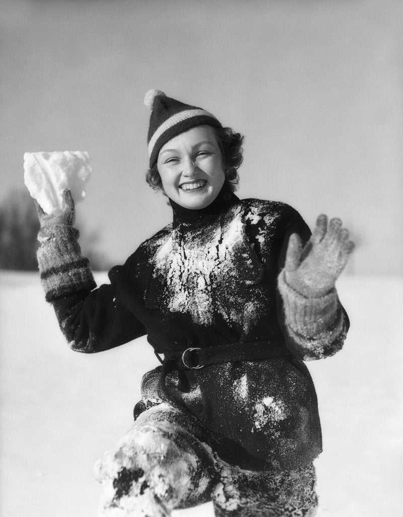Detail of 1930s smiling young woman covered in snow throwing piece of snow squinting looking at camera by Anonymous