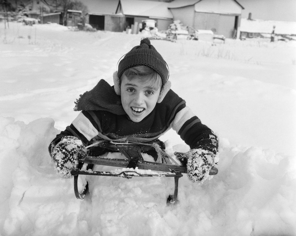 Detail of 1950s boy on sled in snow looking at camera by Anonymous