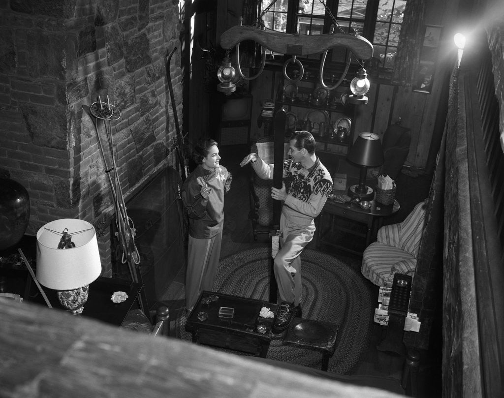 Detail of 1950s couple man woman wearing sweaters talking in ski lodge by fireplace view from above by Anonymous