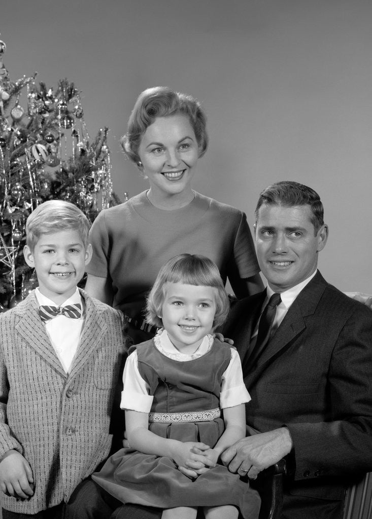 Detail of 1950s 1960s family portrait smiling father mother daughter son sitting together in front of indoor christmas tree by Anonymous