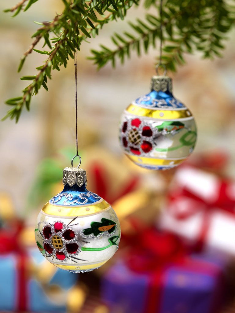 Detail of Close-up of decorated hanging baubles against blurred gifts in the background by Anonymous