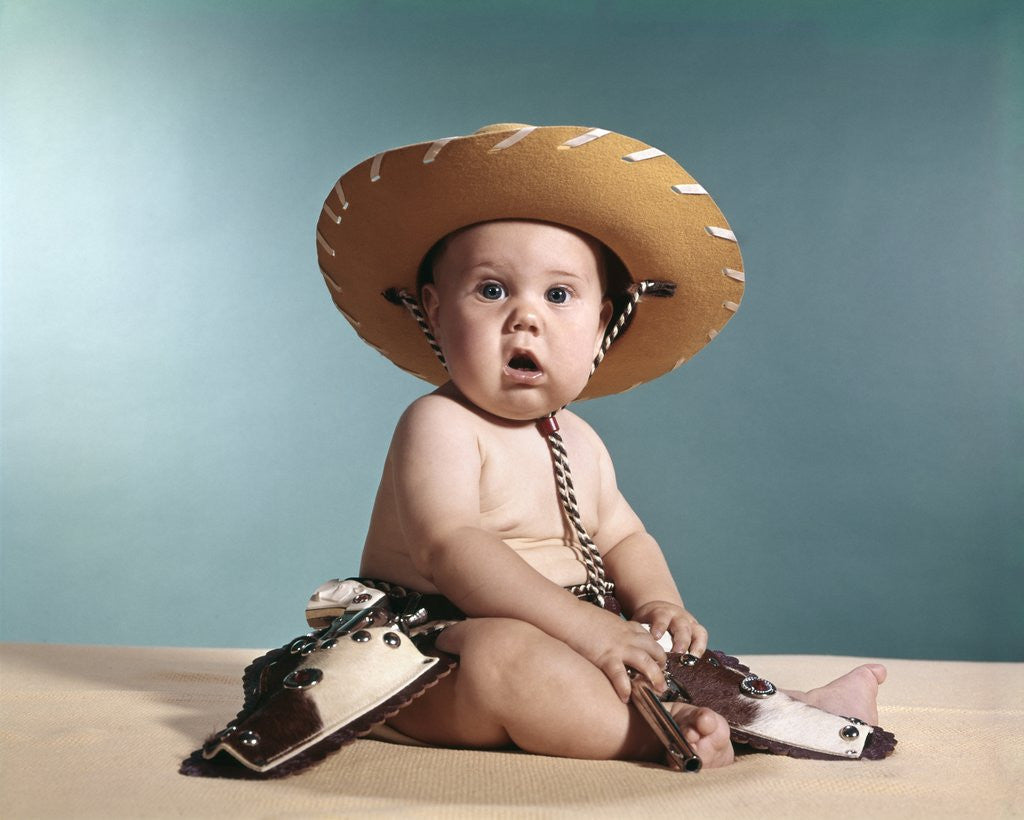 Detail of 1960s Baby Wearing Cowboy Costume With Funny Facial Expression Looking At Camera by Anonymous