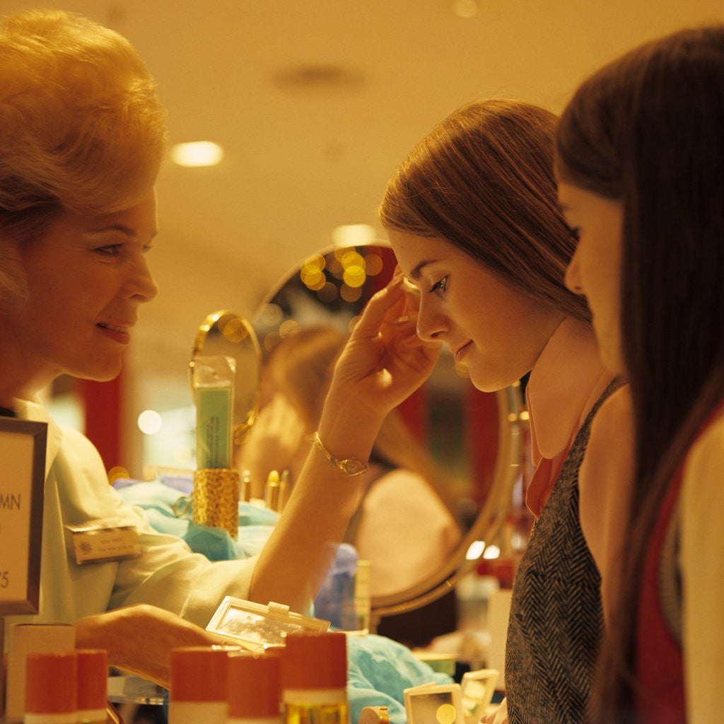 Detail of 1970s Teen Girls At Make Up Counter In Store Having Eye Shadow Applied Tested By Saleswoman by Anonymous
