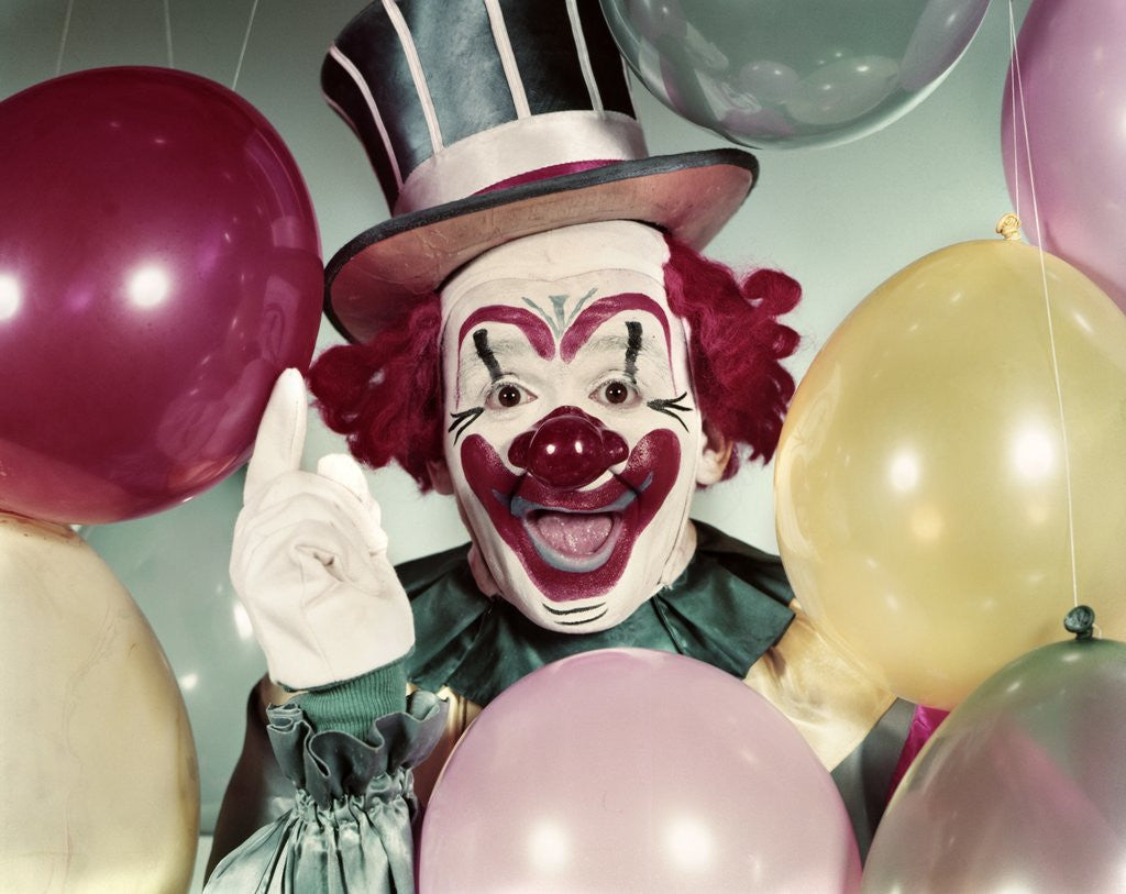 Detail of 1950s Circus Clown Portrait Smiling Amid Balloons Pointing Up Looking At Camera by Corbis