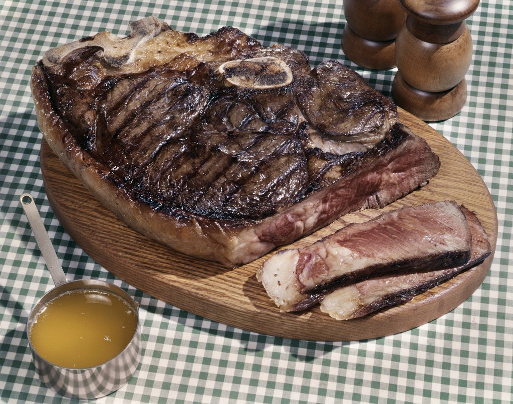 Detail of 1960s Huge Porterhouse Steak On Wooden Platter Sliced Medium Rare Cup Of Drawn Butter Salt Pepper Shakers Green Checked Cloth by Anonymous