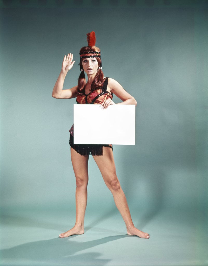 Detail of 1960s 1970s Character Woman Wearing Native American Feather Headdress Making How Gesture Holding Blank Sign Looking At Camera by Corbis
