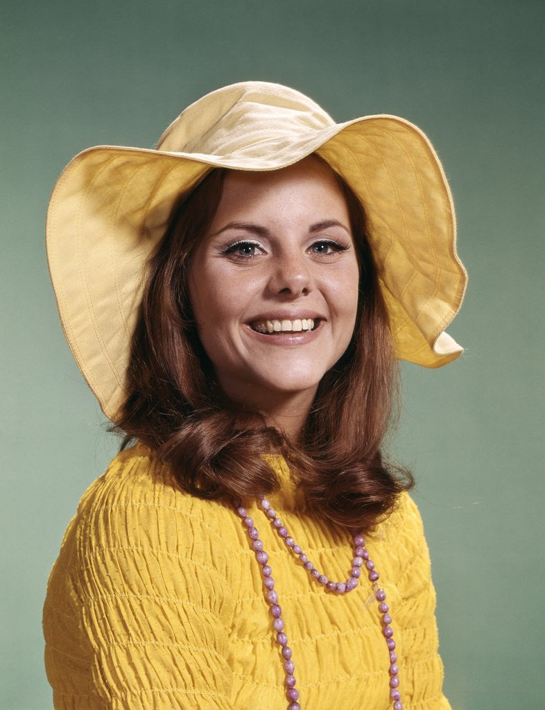Detail of 1970s Smiling Young Woman Wearing Yellow Floppy Brim Hat And Blouse With Pink Beads Looking At Camera by Anonymous