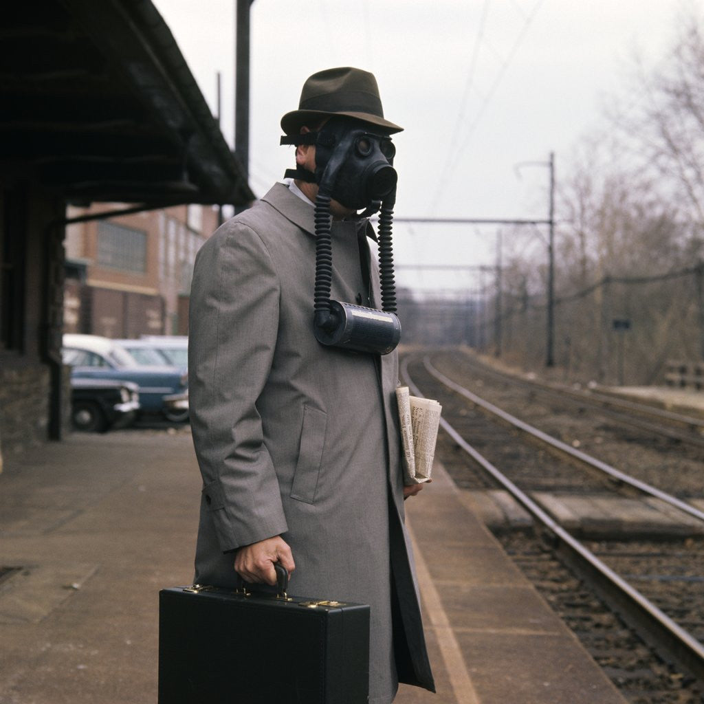Detail of 1950s Man Wearing Gas Mask Hat At Commuter Train Station Holding Briefcase Newspaper by Anonymous