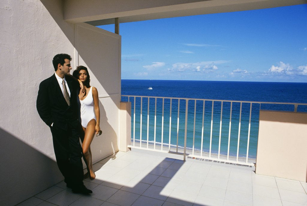 Detail of 1990s Man In Dark Suit And Tie And Woman In White One Piece Bathing Suit Standing Together On Ocean Side Sun Deck by Anonymous