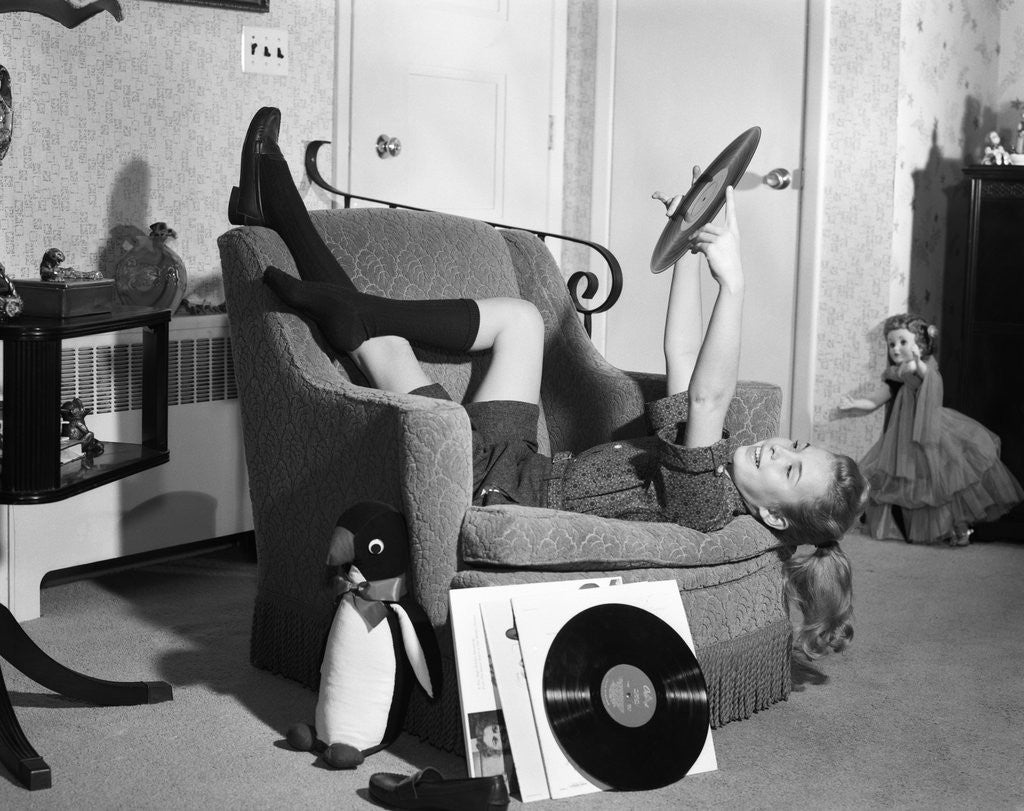 Detail of 1950s 1960s Teenage Girl Smiling Reclining Upside Down On Chair Holding Vinyl Record Album Listening To Music by Anonymous
