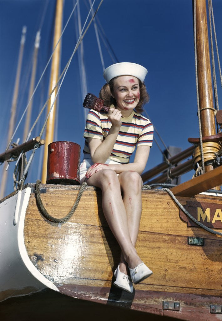 Detail of 1940s Smiling Woman Wearing Nautical Sailor Outfit And Hat Sitting On Edge Of Boat Holding Paint Brush by Corbis