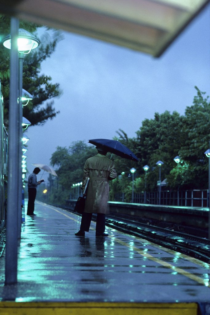 Detail of 1970s 1980s Anonymous Business Man Holding Umbrella Waiting For A Commuter Train by Corbis