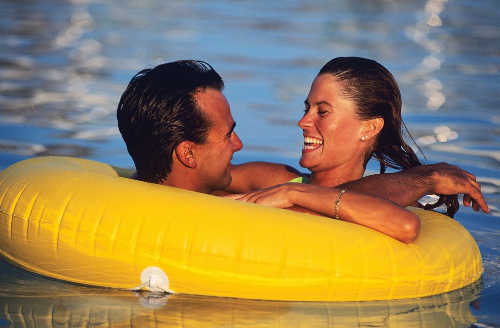 1980s Happy Young Couple Floating Together In Yellow Plastic Inner Tube In A Pool by Corbis