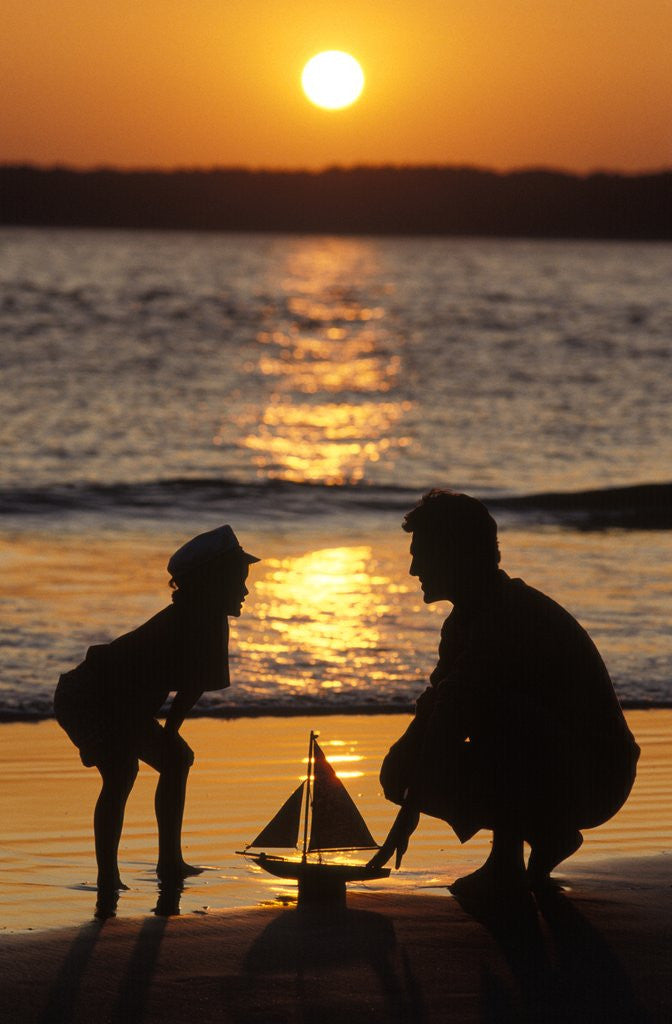 Detail of 1990s Anonymous Father And Son Playing With Toy Boat At The Beach Silhouetted Against Setting Sun by Corbis