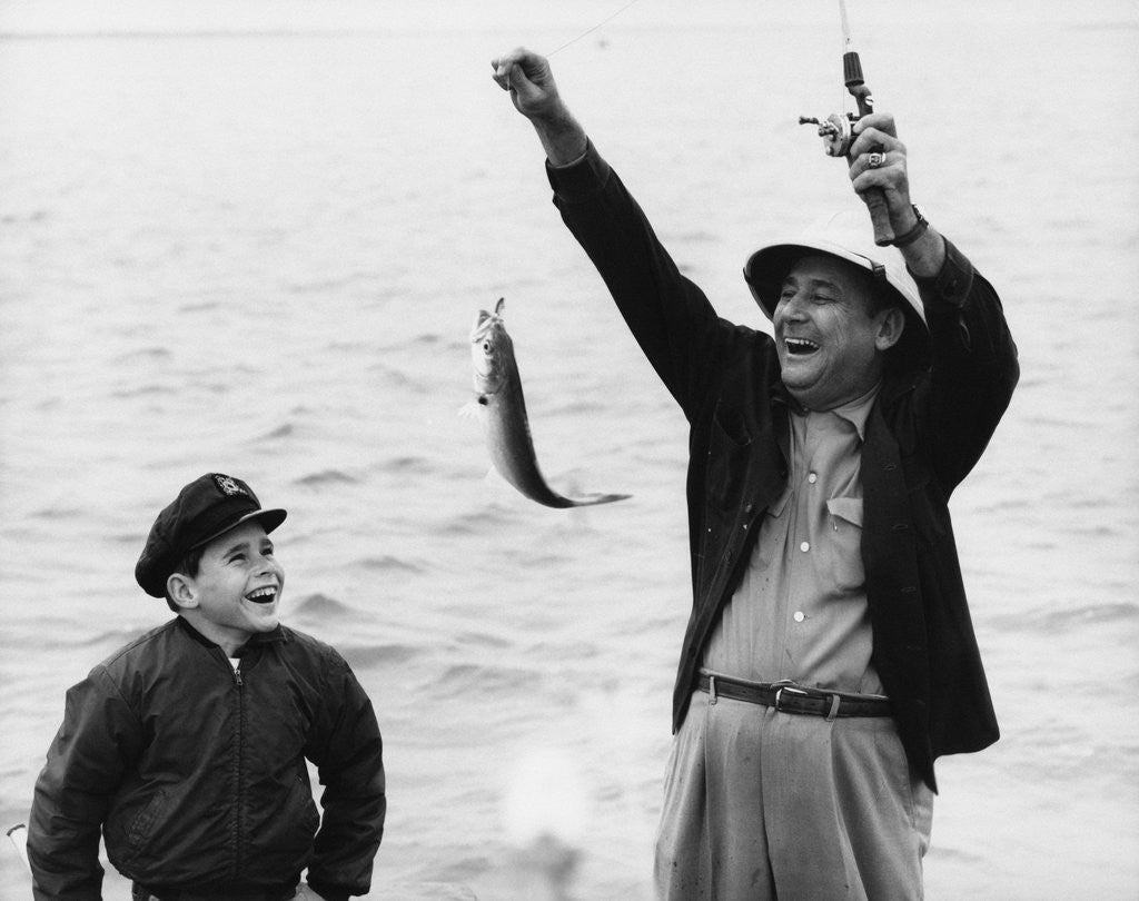 Detail of 1950s 1960s Boy Son Fishing With Man Father Or Grandfather Holding Up Caught Fish On Line Laughing Having Fun by Corbis