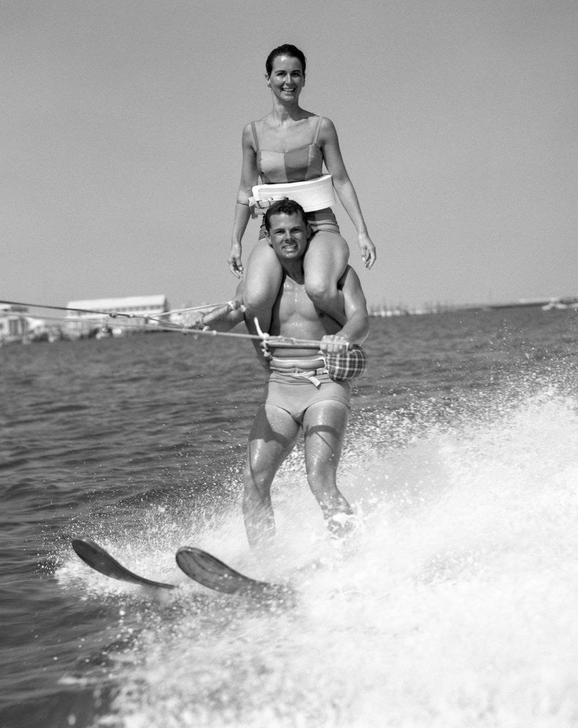 Detail of 1960s Man Water Skiing With Woman In Bathing Suit Riding On Shoulders by Anonymous