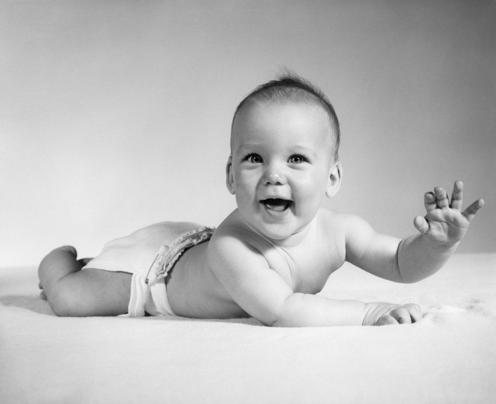 Detail of 1960s Smiling Baby Wearing Cloth Diaper Lying On Stomach Looking At Camera Arm Raised by Anonymous