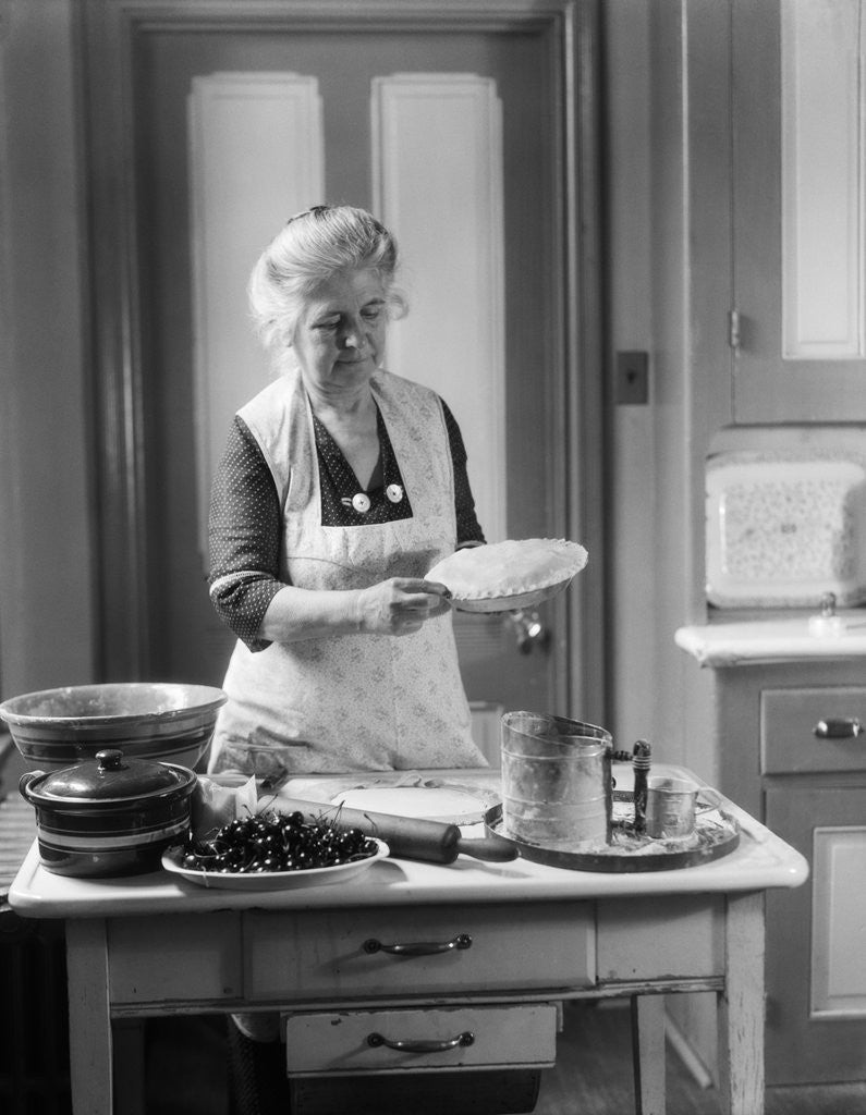 Detail of 1920s 1930s Senior Woman Grandmother Wearing Apron Crimping Crust Making A Cherry Pie In Kitchen by Corbis