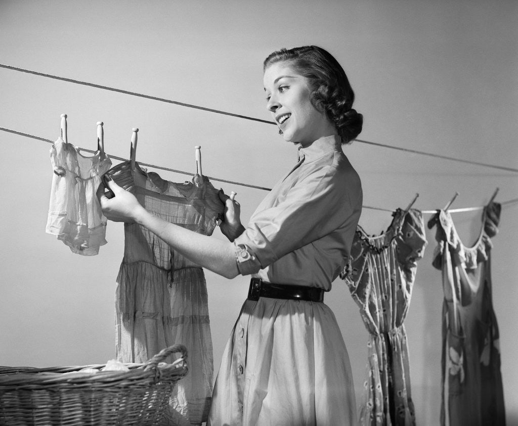 Detail of 1950s Smiling Woman Housewife Hanging Wash Child Dress On Clothesline To Dry by Anonymous