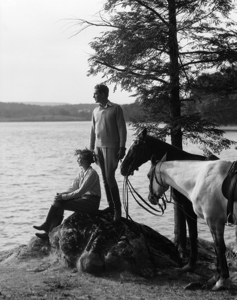 Detail of 1930s Man Standing On Rock Lakeside Holding Reins Of Two Horses With Woman Seated Beside Looking Off To Side by Corbis