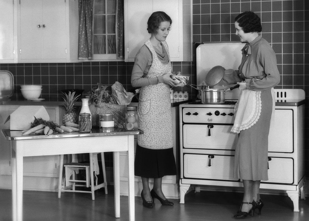 Detail of 1930s Woman Housewife And Friend Wearing Apron Cooking Food In Kitchen On Gas Stove Indoor by Anonymous